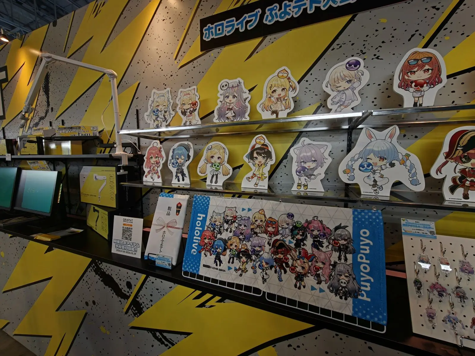 ホロライブぷよテト大会2026のアクリルスタンドとタオルが並ぶ棚